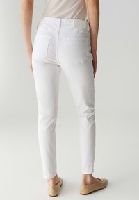 Jeans bianchi slim-fit con una texture liscia e due tasche posteriori. Abbinati a delle ballerine beige, visti da dietro. Design della vita semplice.