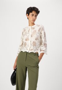 Blonde bluse med blomster mønster, kremfarge, kort design, trekvart ermer og knappeåpning. Kombinert med olivenfargede striped bukser.