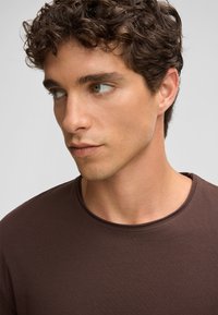 Braunes Rundhals-T-Shirt aus weichem Stoff, mit glatter Textur und minimalen Nähten am Kragen und den Ärmeln.