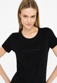 T-shirt nera a maniche corte realizzata in cotone, con un design grafico lucido e borchiato nella parte anteriore. Collo rotondo e vestibilità comoda.