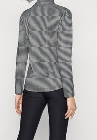 Long-sleeve, mock-neck top in black and white houndstooth pattern, fitted silhouette, soft, stretchy fabric, paired with slim black pants.