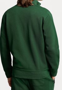 Grön sweatshirt med hög krage, texturerat tyg, ribbade ärmslut och fåll. Har en slank design med en sömlös rygg.