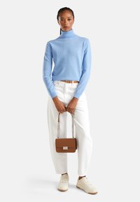 Helles blauer Rollkragenpullover, weiße hoch taillierte Hose, beigefarbene Sneakers und eine kleine braune Handtasche mit Kettenriemen und Metalverschluss.