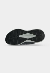 Semelle de sneaker noire et grise avec un motif adhérent texturé et logo "Skechers" au centre sur fond blanc.
