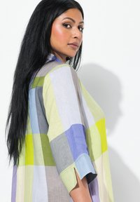 Camicia leggera con bottoni, dal design a quadri, presenta quadrati verdi, blu, grigi e bianchi, con maniche corte e spacchi laterali.
