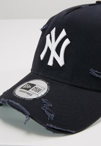 Marineblaue Baseballkappe mit einem weißen gestickten Logo, abgenutztem Stoff, rundem Schirm und verstellbarem Riemen. Enthält ein Markenetikett auf dem Schirm.