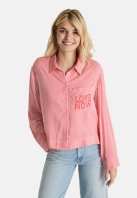 Red and white striped button-up shirt with long sleeves, featuring a pocket embroidered with "LOVE NOW" in red thread.