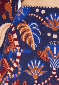 Tissu tricoté présentant un fond bleu marine avec des motifs floraux et de serpents complexes dans des nuances d'orange, de bleu et de crème, mettant en valeur la texture et les détails.