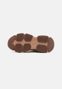 Semelle de chaussure en caoutchouc brun avec un motif de crampons en chevrons distinct et une section centrale lisse, conçue pour l'adhérence et la durabilité.