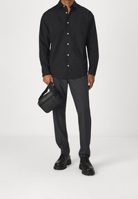 Svart knapp-up skjorta med en framficka, bärs med grå skräddarsydda byxor och svarta läderskor. Håller en liten svart crossbody-väska.