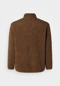Chaqueta de forro polar marrón con una textura suave, un cuello alto y mangas largas con un corte holgado. Sin cierres o adornos visibles.