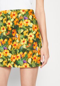Falda Floral con un fondo verde, que presenta flores amarillas y naranjas vibrantes, además de hojas verdes. Ajustada, con un diseño ceñido.