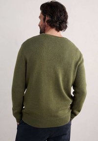 Grön stickad tröja med rund halsringning, ribbade muddar och fåll, med en slät yta och medelvikt. Visningen visar baksidan.