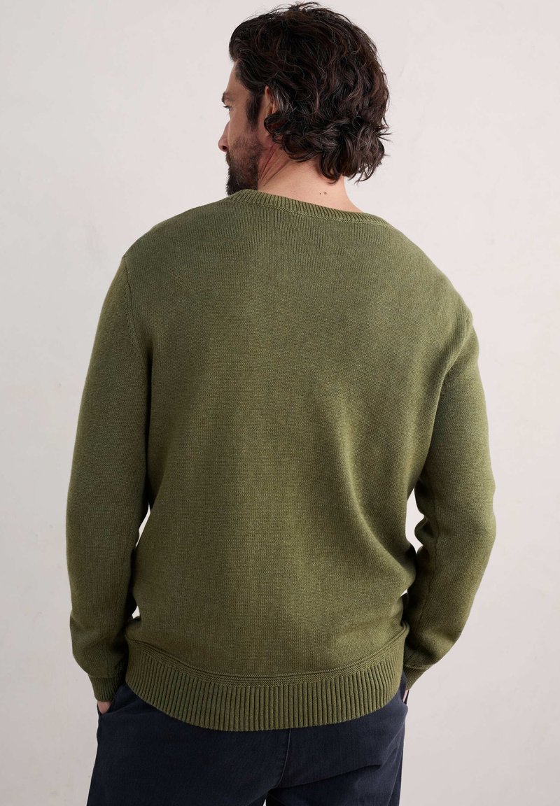 Grön stickad tröja med rund halsringning, ribbade muddar och fåll, med en slät yta och medelvikt. Visningen visar baksidan.