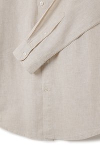 Camisa beige de lino con botones, con dobladillo recto, mangas largas y puños puntiagudos. Cuenta con botones redondos de color claro. Textura suave.