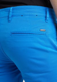 Jasnoniebieskie szorty wykonane z gładkiego materiału, z tylną kieszenią z poziomym otworem i srebrną metką z logo.