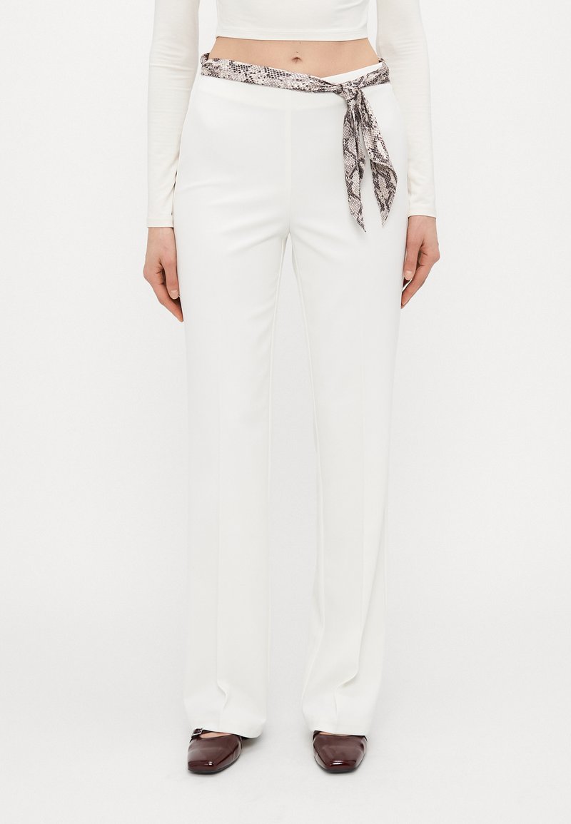 Pantaloni bianchi a gamba larga con una texture liscia e una cintura con stampa a serpente. Scarpe marroni completano l'outfit.