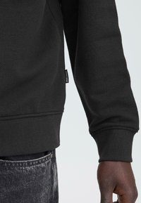 Zwarte gestructureerde sweatshirt met een geribde zoom en manchetten, voorzien van een klein logolabel aan de zijkant en contrasterende gladde stofaccenten.