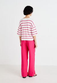 Striped, oversized white and pink top with wide sleeves paired with floor-length pink trousers. Lightweight, casual, and textured fabric.