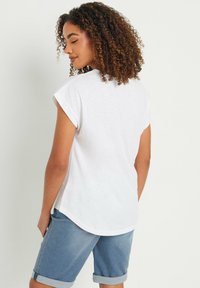 Camiseta blanca de manga corta con puños doblados, dobladillo redondeado y un corte relajado, combinada con pantalones cortos de mezclilla que están doblados por encima de la rodilla.