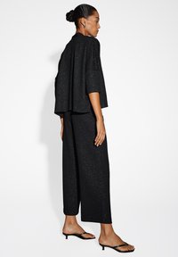 Zwarte two-piece outfit met een losse, kort mouwtop en brede pijpen, beide met subtiele sprankelingen. Sleek zwarte sandalen maken de look compleet.