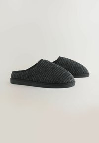 Zwarte geweven slippers met een gestructureerde bovenkant en een ronde teenvorm. Zacht stof, instapstijl en een platte rubberen zool voor comfort.
