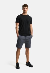Sort bomulds T-shirt med brystlomme, grå shorts og sorte sneakers. Casual pasform, glat tekstur og ensfarvede farver.