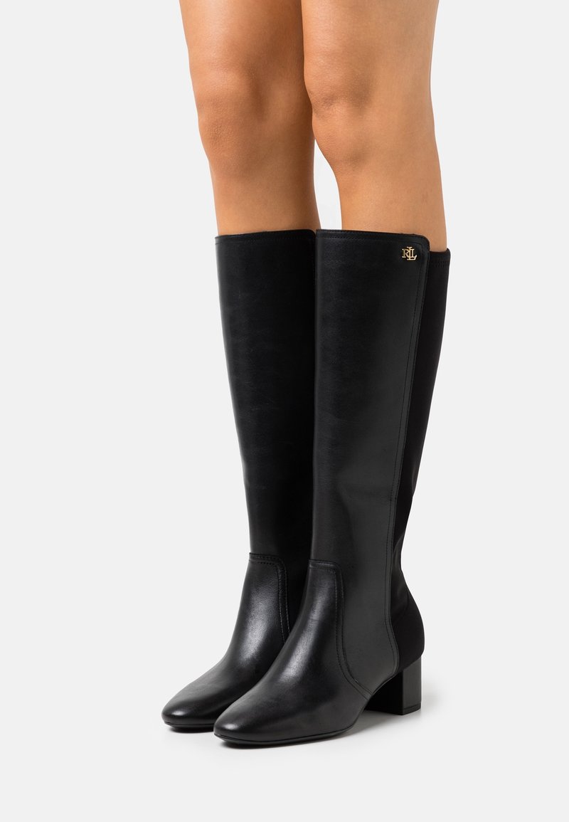 Bottes noires montantes en cuir lisse avec un talon bloc. Elles présentent un subtil logo latéral et un design élégant à bout pointu.