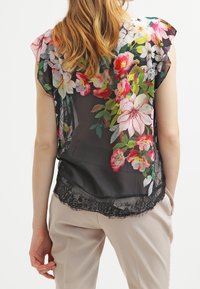 Gennemsigtig sort bluse med farverigt blomsterprint, korte ærmer og blondekant forneden. Blød tekstur og let væv.