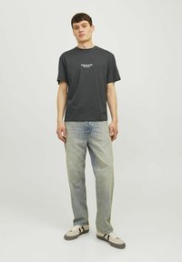 Camiseta de manga corta gris oscuro con texto impreso en blanco, combinada con jeans rectos de pierna clara y zapatillas beige con rayas negras.