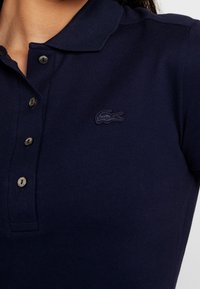 Polo-shirt navy en tissu texturé, avec une patte de boutonnage à trois boutons et un logo de crocodile brodé foncé sur la poitrine.