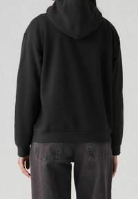 Sweat à capuche noir à coupe ample, doté d'une poche kangourou et de poignets côtelés. Assorti à un jean foncé texturé.