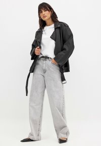 Schwarze Lederjacke mit breitem Kragen über einem weißen T-Shirt, kombiniert mit hochtaillierten, hellgrauen, weiten Jeans und schwarzen Ballerinas.