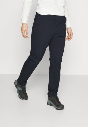 Pantalons bleu marine à coupe droite, fabriqués en tissu léger. Dotés de poches latérales et de coutures discrètes. Associés à des chaussures de randonnée noires.