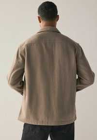 Ruskea villasekoite takki, jossa on rakennettu kaulus, pitkät hihat ja suora leikkaus. Takki on sileä tekstuuri ja siinä on minimaalinen yksityiskohtaus.