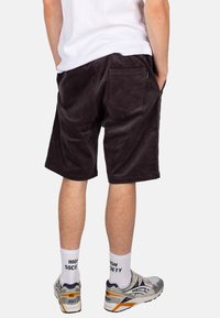 Dunkelbraune corduroy Shorts mit einer Gesäßtasche und strukturiertem Stoff. Kombiniert mit weißen Socken und Sportschuhen.