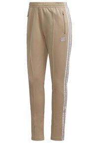 Beiga träningsbyxor med en avsmalnande design, vita sidremsor, dragkedjefickor och elastisk midja. Tillverkade av ett mjukt, stretchigt material.