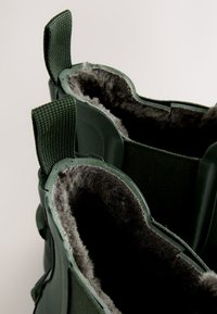 Bottes vert foncé avec une doublure en fausse fourrure grise épaisse et douce et des languettes en tissu à l'arrière, vues de dessus.