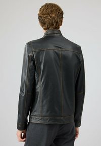 Zwarte leren jas met een gladde textuur, voorzien van een staande kraag en contrasterende bruine stiksels. Ontworpen met een getailleerde pasvorm.