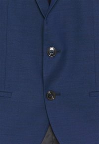 Veste de costume bleu marine en tissu texturé, avec deux boutons noirs, un revers cranté et des poches latérales.