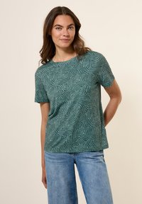 T-shirt vert à manches courtes avec un motif en vagues, col rond et coupe décontractée. Associé à un jean en denim bleu clair.