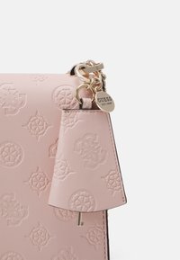 Coin de sac en cuir rose clair avec motif logo embossé, anneaux porte-clés dorés et une plaque métallique ronde gravée GUESS EST.1981.