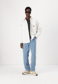 Valgest ja hallist triibulisest oversized särgist, mustast T-särgist, helesinistest teksapükstest ja beežidest sportlike jalanõudest koosnev komplekt. Mustad prillid täiustavad välimust.