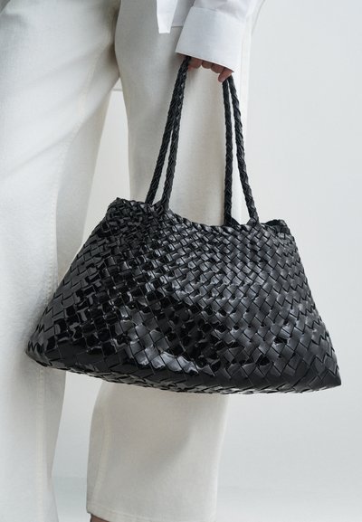 Juodas pintas rankinė su pynėmis, turintis blizgesį ir trikampį dydį, derinamas su šviesiais kelnėmis.