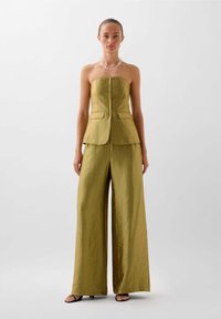 Gul strapless peplum-top med to frontlommer, parret med brede bukser lavet af et tekstureret, skinnende stof. Svarte sandaler fuldender looket.