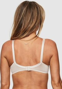 Ljus beige bh med justerbara band och en slät yta. Har en hake-och-öga-stängning och delikata vågiga kanter.