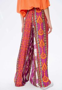Spodnie o szerokich nogawkach charakteryzują się wyrazistym wzorem w fioletowe, pomarańczowe i czarne paski. Wykonane z lekkiego materiału, mają luźny krój i swobodny fason.