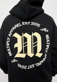 Sudadera negra con un gran logo en blanco y amarillo en la parte posterior, que presenta el texto "MULTIPLY APPAREL EST 2015" y detalles de diseño de fuente únicos.