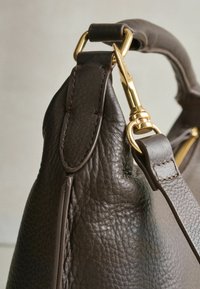 Ruskea nahkainen käsilaukku, jossa on teksturoidu viimeistely ja kultaisenvärinen metalliklipsi sekä hihnan kiinnike turvallista pitoa varten.