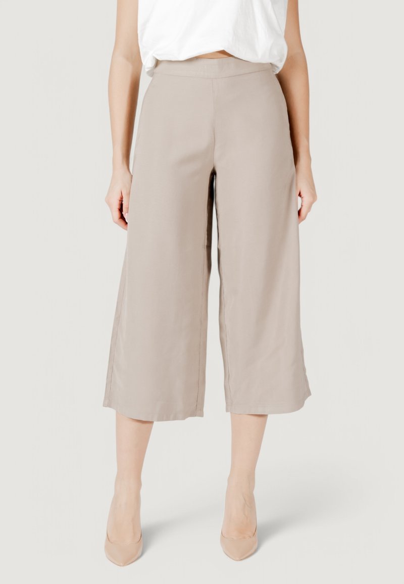 Pantalones beige de pierna ancha con una textura suave, cinturilla de altura media y corte a la altura del tobillo, combinados con tacones nude.